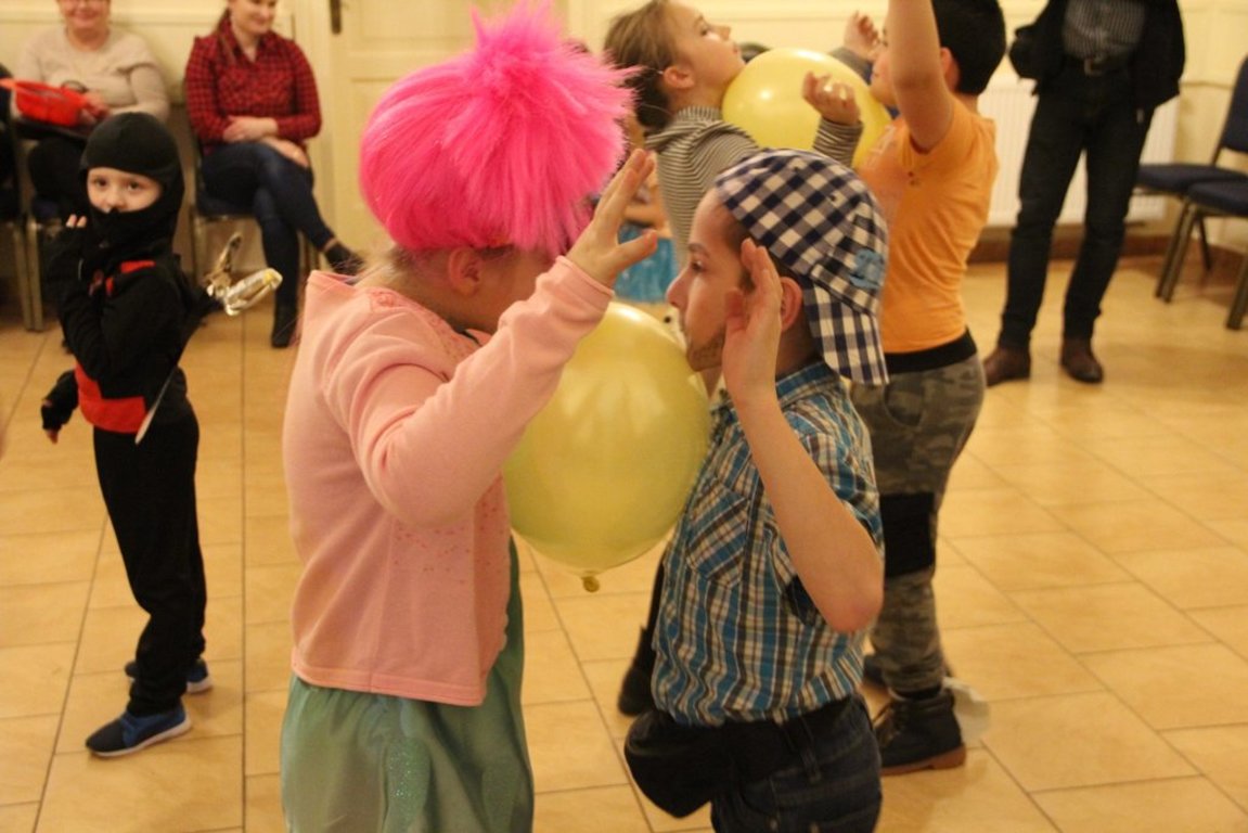 Dwoje dzieciaków na pierwszym planie trzymających balon między sobą tańczą