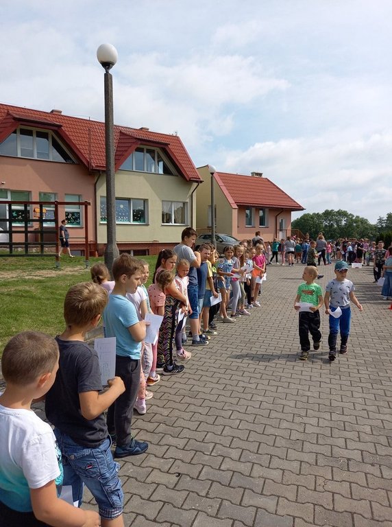 Dzieci przed budynkiem szkoły stojący w grupach oczekujący do zabaw