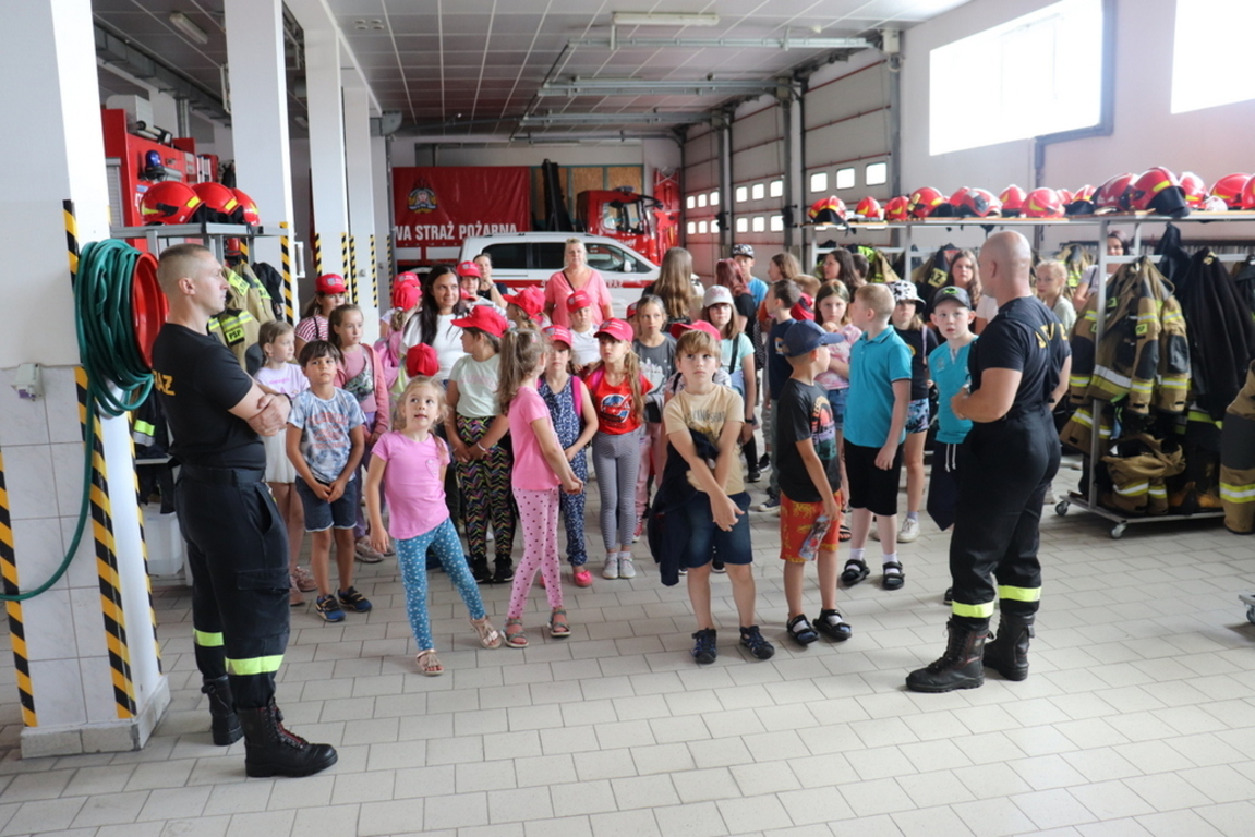 Zdjęcie zrobione w garażu Komendy PSP Lipno. Strażacy prowadzą zajęcia edukacyjne. Obok grupka dzieci.