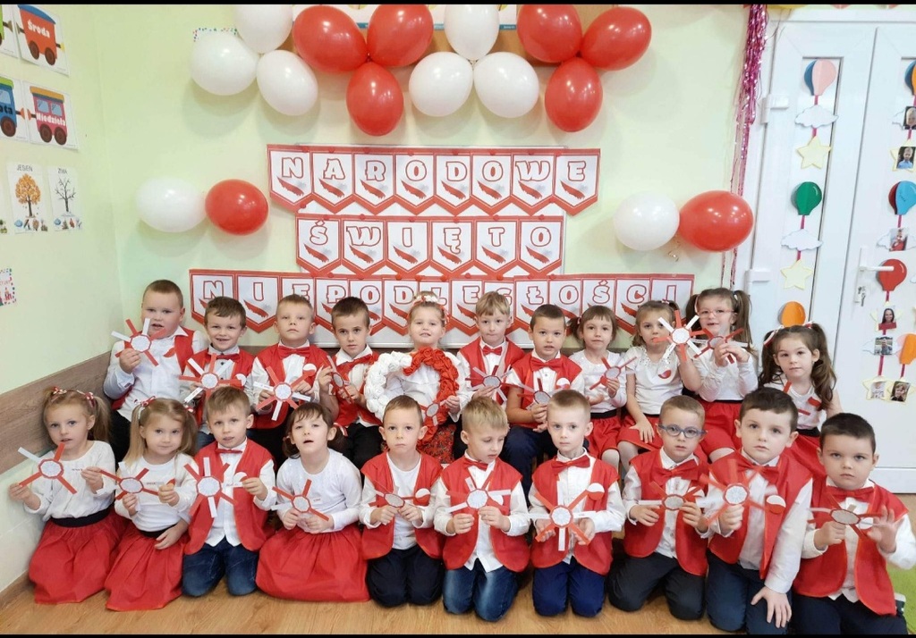 Dzieci z grupy "Biedronki" przy tablicy tematycznej ze zrobionymi przez siebie kotylionami.