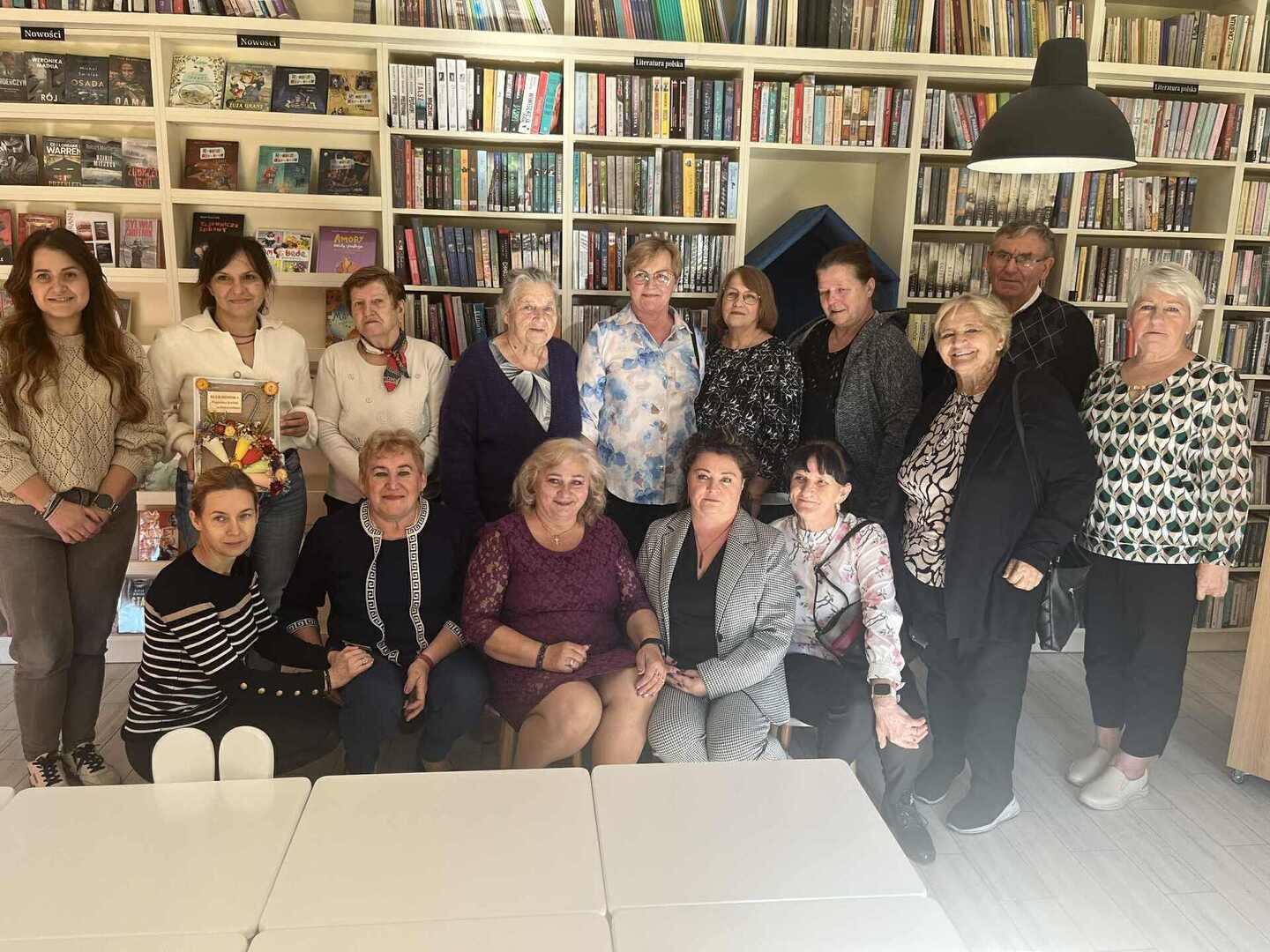 Zdjęcie grupowe seniorów i bibliotekarzy w tle regały z książkami