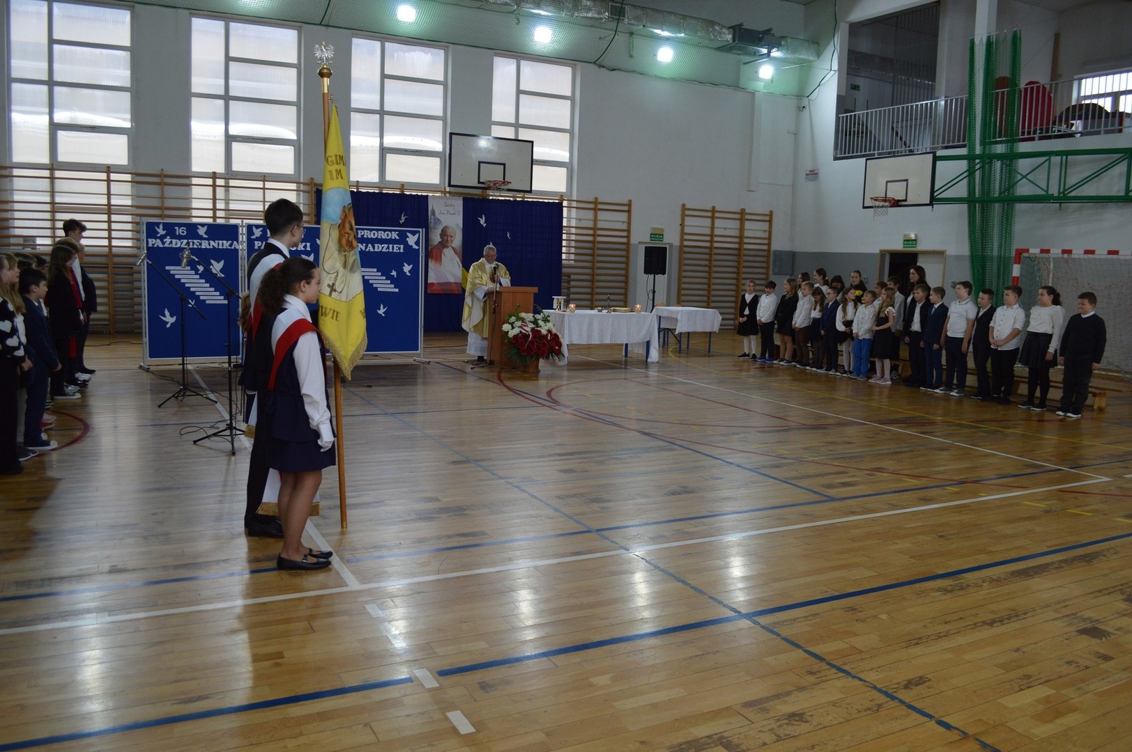 Społeczność szkolna uczestniczy w mszy świętej. Na środku kapłan odprawiający mszę, po bokach uczniowie.