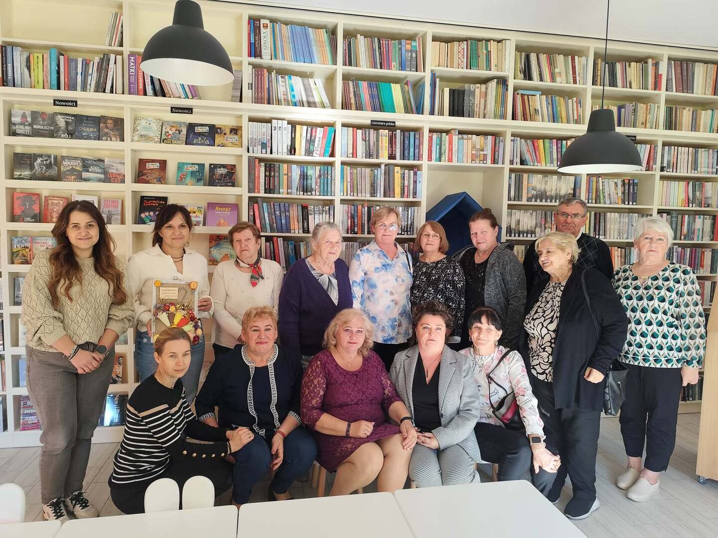 Zdjęcie grupowe seniorów na tle biblioteki.