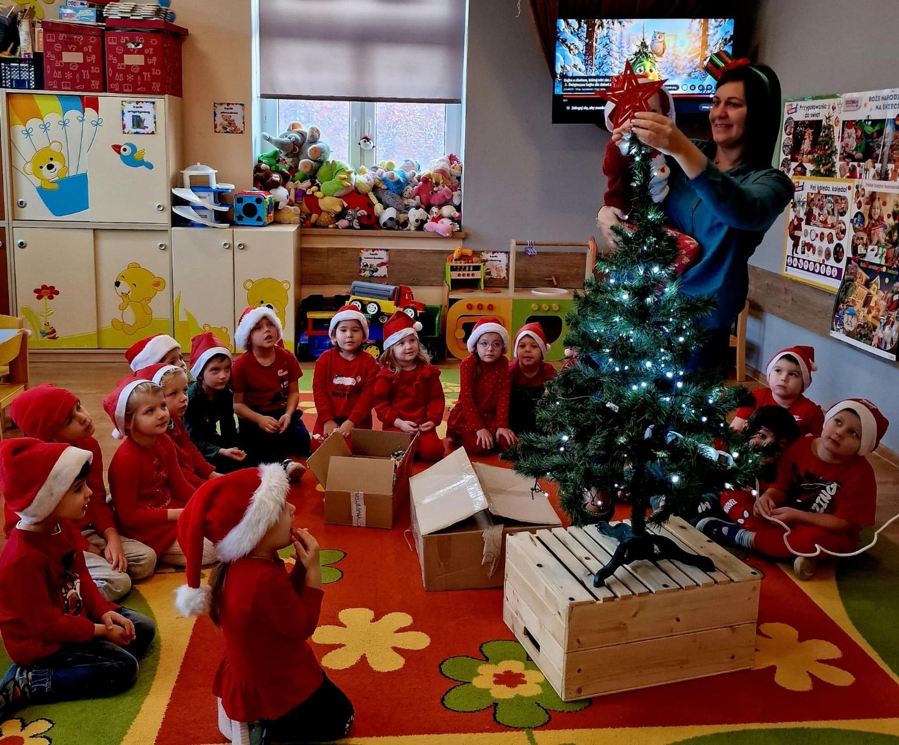 Dzieci siedzą na dywanie, bibliotekarka zakłada gwiazdę na choinkę