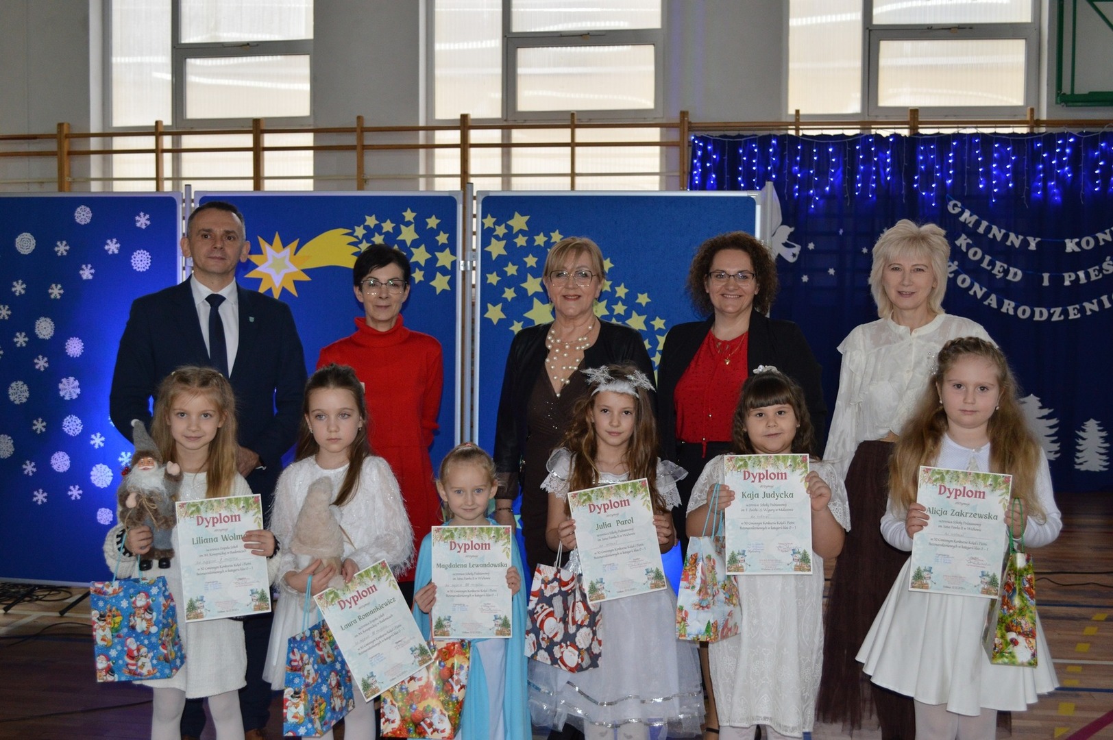 Zdjęcie przedstawia laureatów konkursu kolęd, wraz z jury i organizatorami. Dzieci w ręku trzymają dyplomy i nagrody.