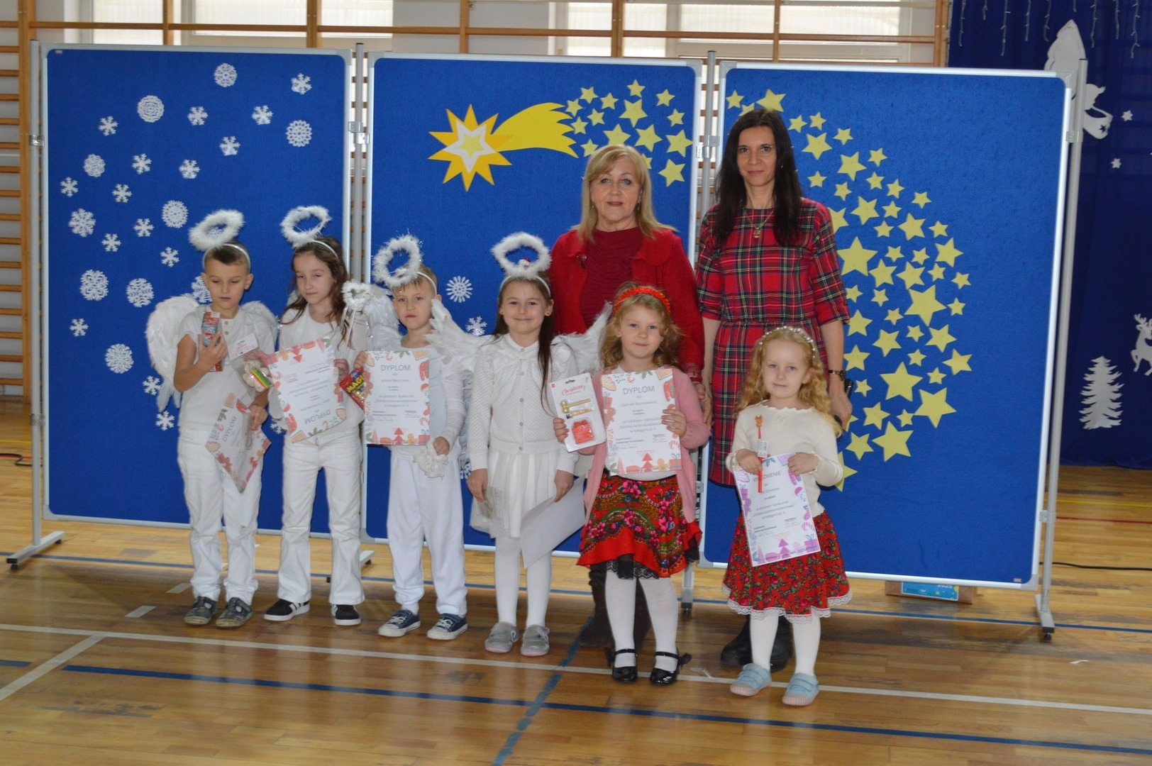 Na zdjęciu małe dzieci: laureaci konkursu „Ozdoba bożonarodzeniowa” w kategorii kl. 0, z tyłu dwie kobiety; dyrektor szkoły i organizatorka konkursu.