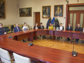 Grupa młodzieży oraz dorosłych siedząca przy stołach na auli Urzędu Miejskiego