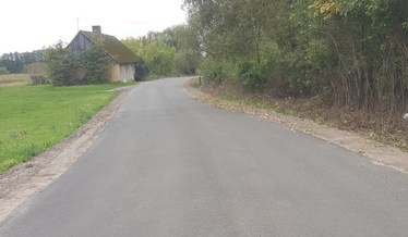 Sceneria jesienna. Zdjęcie przedstawia nowo wykonaną drogę przebiegającą wzdłuż lasu a w oddali po l