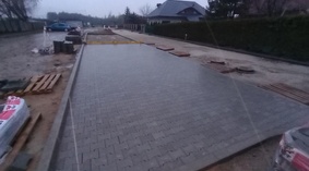 Układanie kostki brukowej na parkingu wzdłuż drogi dojazdowej do boiska sportowego.
