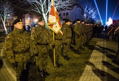 Żołnierze stojący w szeregu ze sztandarem, biorący udział w uroczystościach.