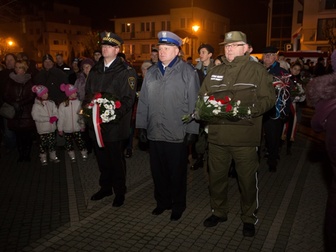 Przedstawiciele służb mundurowych składający wiązankę kwiatów pod pomnikiem.