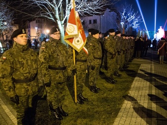Żołnierze stojący w szeregu ze sztandarem, biorący udział w uroczystościach.