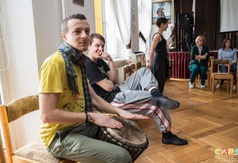Mężczyzna grający na bębnie, prowadząca oraz uczestnicy w trakcie ćwiczeń podczas warsztatów teatral
