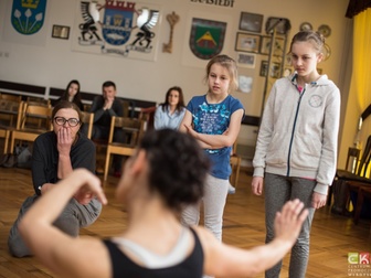 Uczestnicy spoglądający na prowadzącą w trakcie ćwiczeń podczas warsztatów teatralnych.